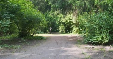 Elbiseli bir kız yeşil ağaçların arasında parktaki toprak yolda elektrikli scooter kullanıyor. Çevre taşımacılığı konsepti, geleceğin köyü. Yüksek kalite 4k görüntü