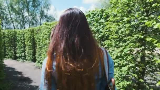 若い女性は緑の背の高い茂みの迷路を歩く カメラは後ろから彼女を追いかける 春の夏 新しい何かを模索しながら忍び込むというコンセプト — ストック動画