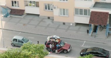 Taşınmak için arabayı aile yükledi. Çatı rafında bağlı eşyalar var. Büyük bir yolculuk için eşyaları topluyorum. Üst manzara, şehir, girişin altındaki park yeri. Sonsuza dek taşınıyorum. Yüksek kalite 4k görüntü