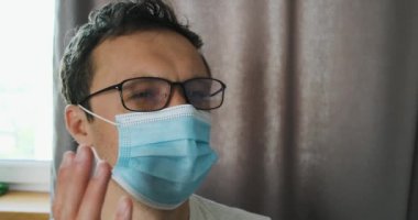 Yüzünde tıbbi maske olan adam gözlüğü buğulanmış. Gözlüklerini temizlemek için çıkarıyor. Yakın plan, portre. Koruma, iş, sağlık personeli ve doktor sıkıntısı kavramı