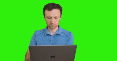 Genç, beyaz bir adam dizüstü bilgisayarla çalışıyor. Ön manzara, portre, yeşil ekran, kroma anahtarı. Çevrimiçi çalışma, uzaktan çalışma, yazışma, web sörfü, blog yazma kavramı. Yüksek kalite 4k görüntü