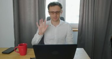 Adam dizüstü bilgisayarın önünde oturuyor ve video aracılığıyla iletişim kuruyor. Mesafe öğrenme, çalışma, iletişim, konuşma, web kamerası konsepti. Portre, ön manzara, iç mekan. Yüksek kalite 4k