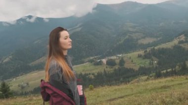 Dişi, arka planda yeşil çimlerde yürüyor. Beyaz bulutlarla kaplı güzel dağlar. Sihirli manzara, dağ köyü, yan manzara. Seyahat kavramı, hedefe git, kendinden emin, güçlü, bağımsız.