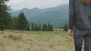 A young long-haired girl walks through a clearing, looking at the mountains ahead. Green forest, wide shot, rear view, daytime, cloudy. Carpathians, Ukraine. High quality 4k footage