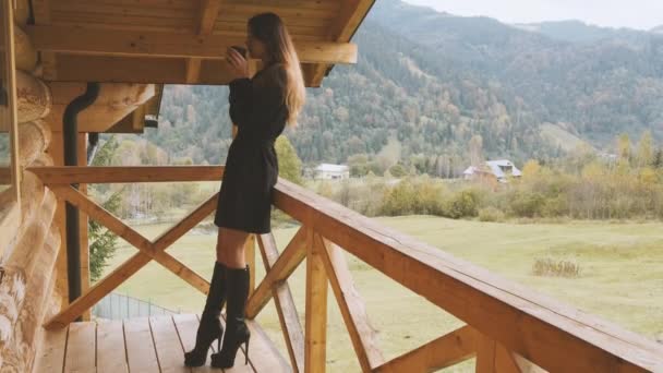 Stylowa Kobieta Czarnych Butach Stoi Drewnianym Tarasie Hotelowym Balkonie Pije — Wideo stockowe