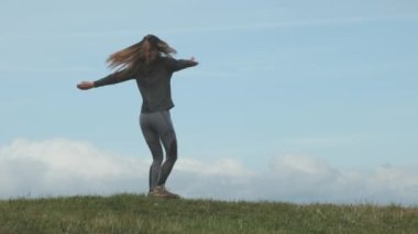 Long-haired girl on hill spins around herself. Happy hiker in mountains against sky. Concept of carelessness, dizziness, conquering peaks, achieving goals, goal achievement, health, sport. High