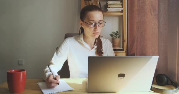 Female Student Glasses Studies Home Front Laptop Writes Notes Notebook — Stockvideo