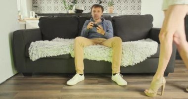 Girlfriend takes gamepad from guy. Gamer on couch plays video game. Unrecognizable woman with long legs comes and interrupts the fun of the game. Concept of gambling, attracting attention