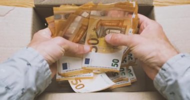 Hands pick up a bunch of 50 euro banknotes from a cardboard box. Top view, pov. The concept of savings, savings, break the piggy bank. High quality 4k footage