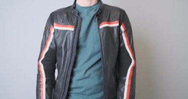 Biker in a leather black sports motorcycle jacket, holds a plastic back protection in his hands, demonstrates it, squeezes it. Front view, close-up, indoors. High quality 4k footage