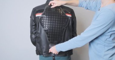 A woman applies a back protector to a leather motorcycle sport jacket worn by a biker. Moto accessories, saving the life of a motorcyclist. Fitting protection, rear view, close-up. High quality 4k
