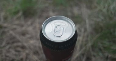 Womens hands open a can of beer standing on the grass. Side view from above. The foam protrudes beyond the edges of the can. High quality 4k footage