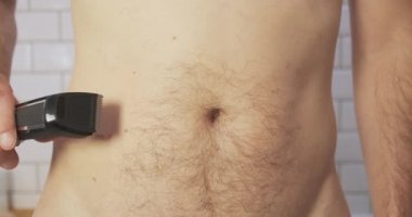 Man removes hair on his belly with an electric clipper, trimmer. Front view, close-up, bathroom. High quality 4k footage