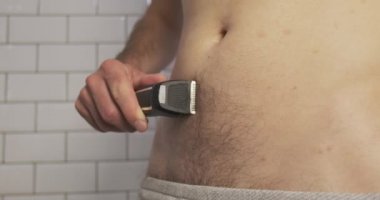 Male shaves his belly with a trimmer. Side view, close-up, bathroom. Body care, male beauty, smooth skin. High quality 4k footage