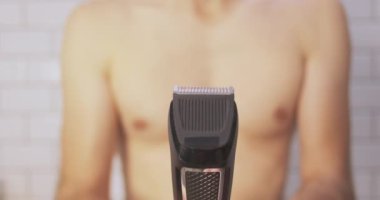 Trimmer close-up. A man starts to shave his chest against the background, blurry, of a bathroom. Personal care, male beauty, metrosexual. High quality 4k footage