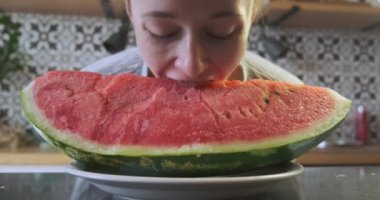 Young girl with braces bites a huge piece of juicy watermelon lying on a plate in the kitchen. High quality 4k footage