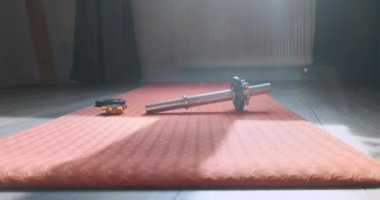 Disassembled metal dumbbell lies on an orange yoga mat in the room. The camera zooms in on the dumbbell. High quality 4k footage