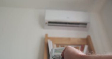 Mans hand presses the buttons on the remote control from the air conditioner. Blurred white air conditioner on background. High quality 4k footage