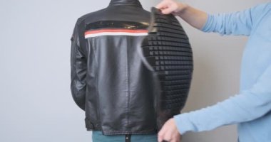 Trying on a plastic back protector for a motorcycle jacket. A girl puts a stove on the back of a biker dressed in a leather motorcycle jacket. High quality 4k footage