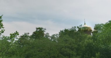 The golden dome of the Christian church among the green branches of trees. Daytime, cloudy, sky. High quality 4k footage
