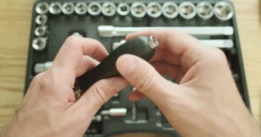 Auto mechanic connects a screwdriver and a ratchet wrench, demonstrates how it works. A set of socket heads and bits lies on the table. Top view, first person view. High quality 4k footage