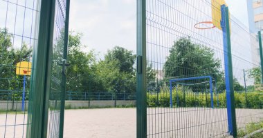 Basketball hoop behind the fence, courtyard of a residential area. Multi-storey residential buildings, green trees, bushes. Kyiv, Ukraine. High quality photo