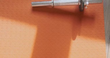 Disassembled metal dumbbell lies on an orange yoga mat in the room. Disassembled metal dumbbell lies on an orange yoga mat in the room. Top view. High quality 4k footage