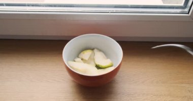 plate with chopped pear slices. A mans hand takes one piece with a fork. Point of view. Window sill, window. Vegetarian, raw foodist. High quality 4k footage
