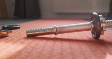 Disassembled metal dumbbell lies on an orange yoga mat in the room. The camera zooms in on the dumbbell. High quality 4k footage