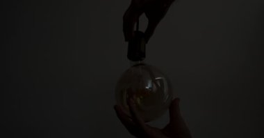 Male hands screw a light bulb into a socket in a dark room. Close-up. Yellow bright light, the light bulb on the wire lights up. High quality 4k footage