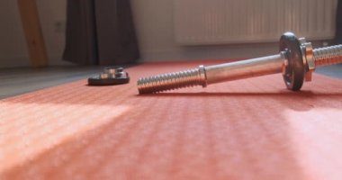 Disassembled metal dumbbell lies on an orange yoga mat in the room. Panorama at home, beam of light falls on a metal. High quality 4k footage