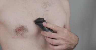Young caucasian man shaving his chest with a trimmer. Side view, close-up. High quality 4k footage