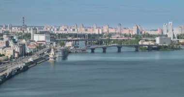 Şehrin binalarının manzarası. Köprüleri olan geniş bir nehir. Yollarda araba trafiği. Geniş açı, gündüz, mavi gökyüzü. Avrupa, Ukrayna, Kyiv. Yüksek kalite 4k görüntü