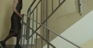 Elbiseli sarhoş genç kız evine dönüyor. Konut binasının beton basamaklarına tırmanmak, sarsıcı. Yan görüş. Bir el çantası ve bir şişe alkolün ellerinde. Yüksek kalite 4k görüntü