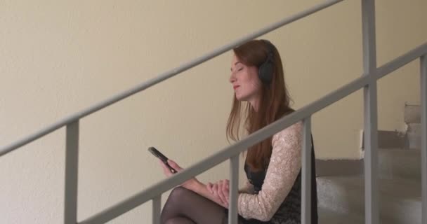 Белая Молодая Женщина Слушает Музыку Наушниках Смотрит Экран Смартфона Лестница — стоковое видео