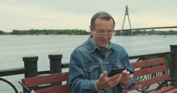 Ein Älterer Mann Nutzt Ein Smartphone Vorderansicht Holzbank Park Breiter — Stockvideo