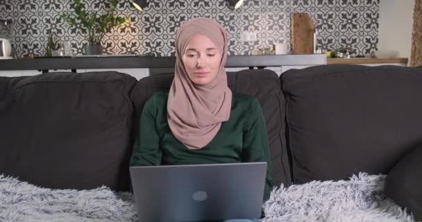 穿着头巾的年轻漂亮女士坐在客厅的沙发上 在笔记本电脑上工作 相机在脸上放大了 在家工作的概念 在线学习 自由职业 — 图库视频影像