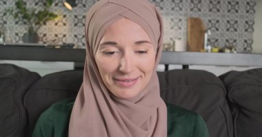 Tesettürdeki kadın gülümsemesi dikkatlice aşağı bakar, portre, oturma odası. Bilgisayarda çalışma kavramı, öğrenme, uzaktan çalışma, serbest çalışma. Yüksek kalite 4k görüntü