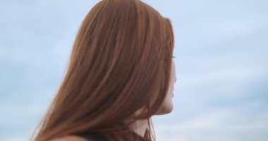 Kızıl saçlı genç bayan bulutlu bir gökyüzüne karşı düşünceli bir şekilde uzaklaşıyor. Yatıştırma, sükunet, huzur, endişe kavramı. Yüksek kalite 4k görüntü