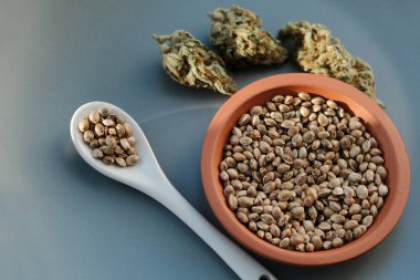Birkaç tomurcukla birlikte bir kaşık ve tabakta bir demet kenevir tohumu yatıyor.