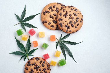 Marmelat ve esrarlı Amerikan kurabiyeleri. CBD yağlı tatlılar. Beyaz arka planda marihuana yaprakları. Üst manzara, düz uzanma.