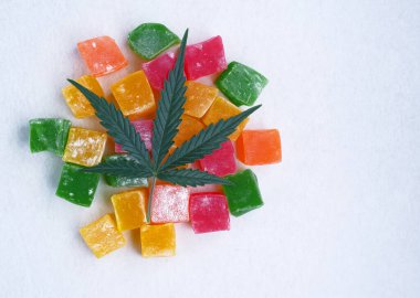Renkli marmelat ve marihuana yaprağının beyaz dokulu arka planı. CBD yağlı tatlılar. Üst manzara, düz uzanma.