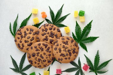 Esrar özlü Amerikan kurabiyeleri. CBD yağlı tatlılar. Beyaz arka planda marihuana yaprakları. Üst manzara, düz uzanma.