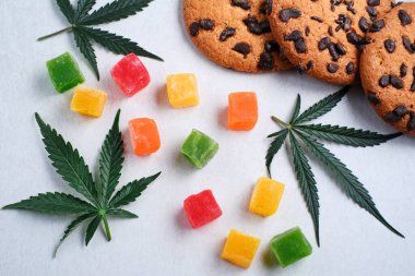 Marmelat ve esrarlı Amerikan kurabiyeleri. CBD yağlı tatlılar. Beyaz arka planda marihuana yaprakları. Üst manzara, düz uzanma.