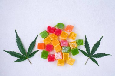 Renkli marmelat ve marihuana yaprağının beyaz dokulu arka planı. CBD yağlı tatlılar. Üst manzara, düz uzanma.