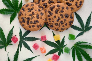 Esrar özlü Amerikan kurabiyeleri. CBD yağlı tatlılar. Beyaz arka planda marihuana yaprakları. Üst manzara, düz uzanma.