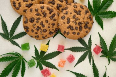 Esrar özlü Amerikan kurabiyeleri. CBD yağlı tatlılar. Beyaz arka planda marihuana yaprakları. Üst manzara, düz uzanma.