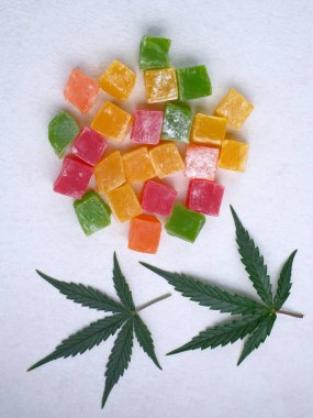 Renkli marmelat ve marihuana yaprağının beyaz dokulu arka planı. CBD yağlı tatlılar. Üst manzara, düz uzanma.