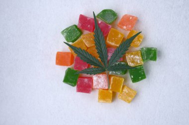 Renkli marmelat ve marihuana yaprağının beyaz dokulu arka planı. CBD yağlı tatlılar. Üst manzara, düz uzanma.