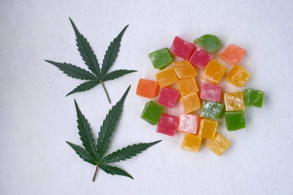 Renkli marmelat ve marihuana yaprağının beyaz dokulu arka planı. CBD yağlı tatlılar. Üst manzara, düz uzanma.